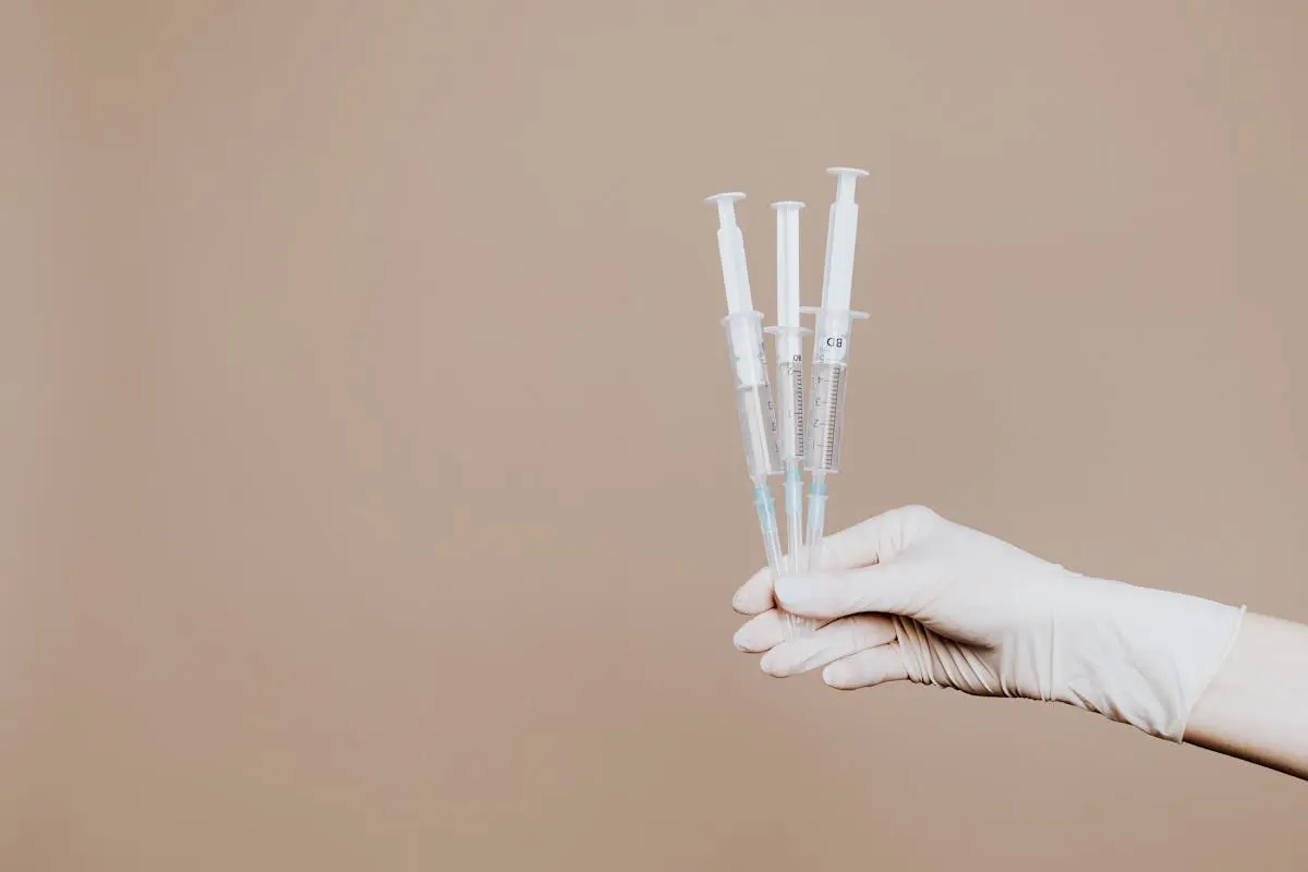 A gloved hand holds three sterile syringes, symbolizing healthcare and vaccination.