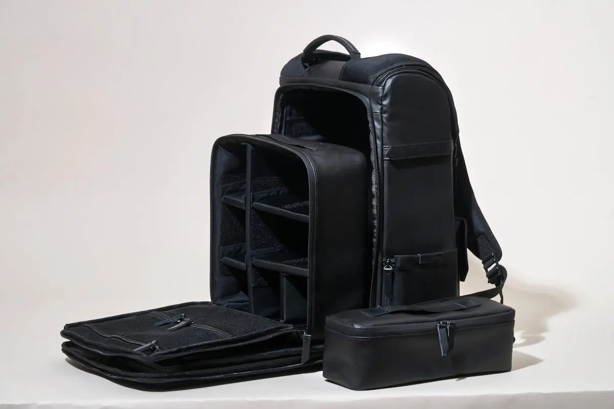 Sleek black leather camera Carry On Backpack showcasing compartments on a white background.