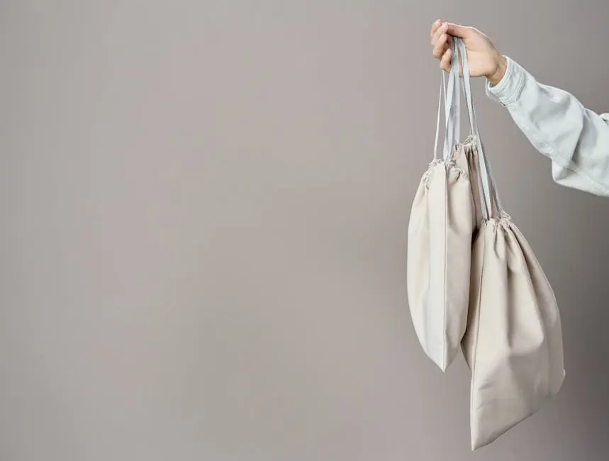 Hand holding eco-friendly canvas bags against a neutral background, ideal for sustainable themes.