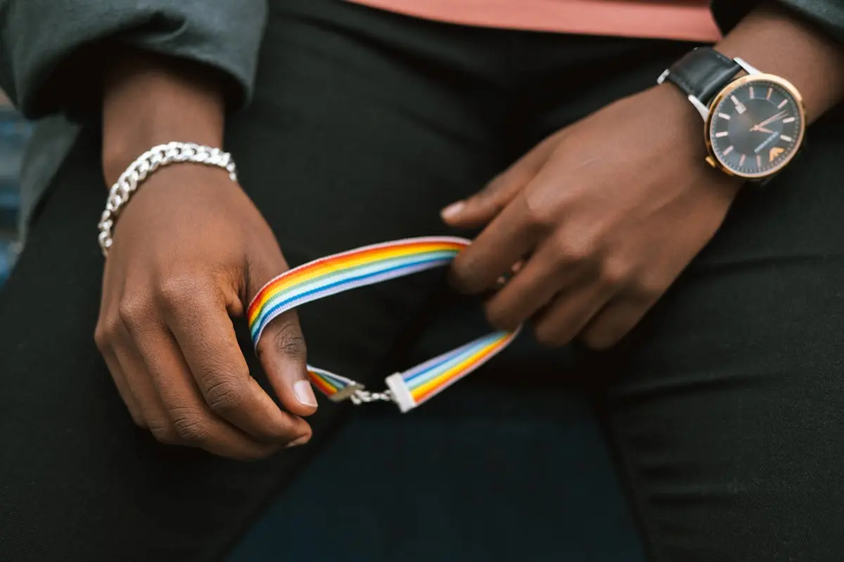 Crop anonymous African American homosexual male in casual clothes holding bright gay bracelet