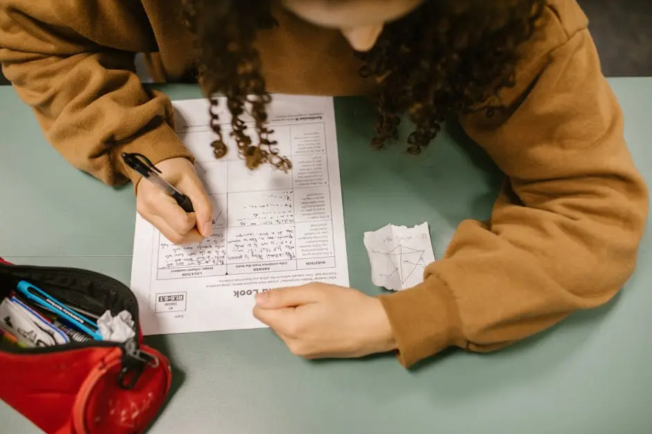 Overhead view of a student writing an exam with a cheat sheet on the desk.