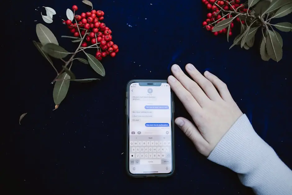 A hand beside a smartphone showing a text message conversation, surrounded by red berries.