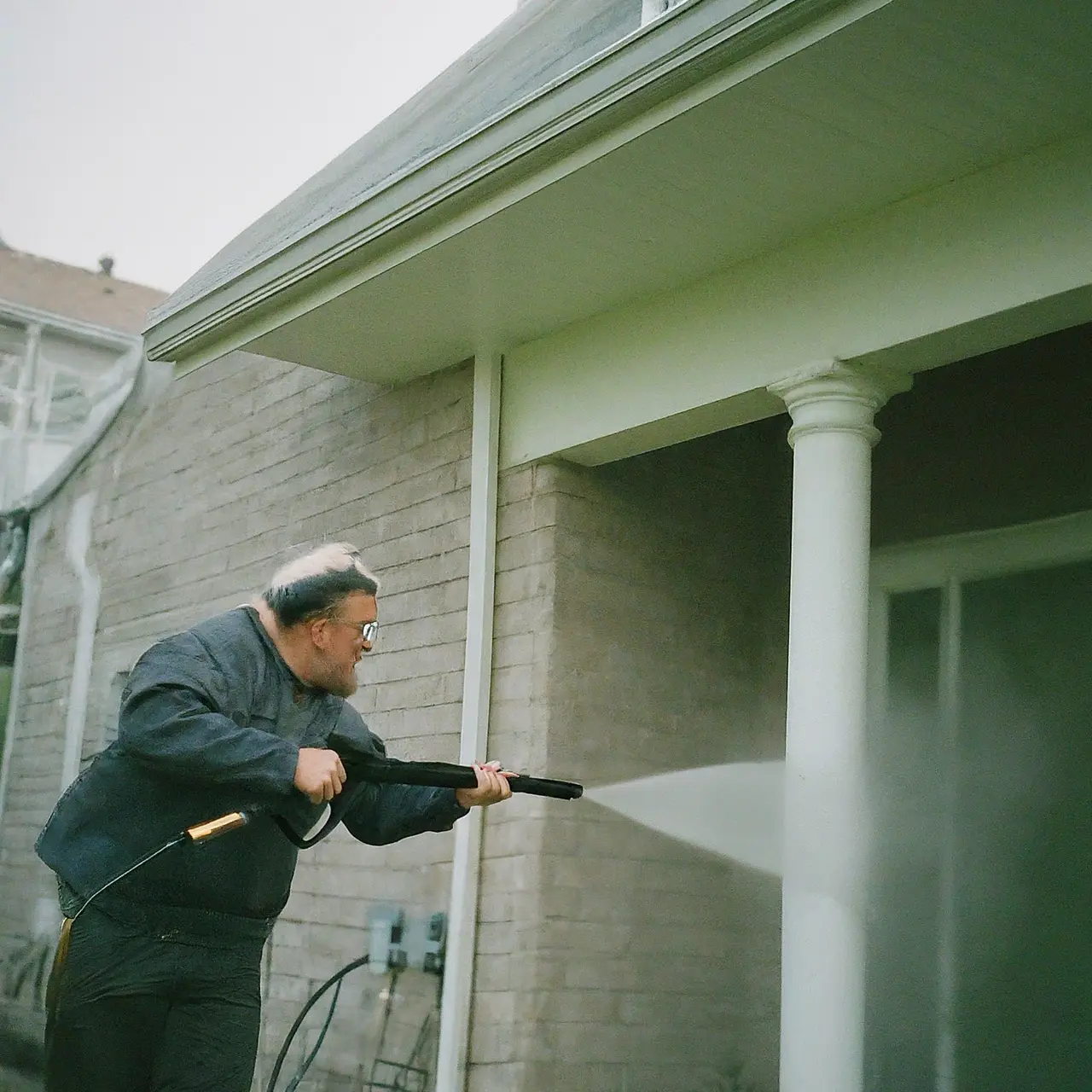 A professional pressure washer cleaning a house exterior. 35mm stock photo