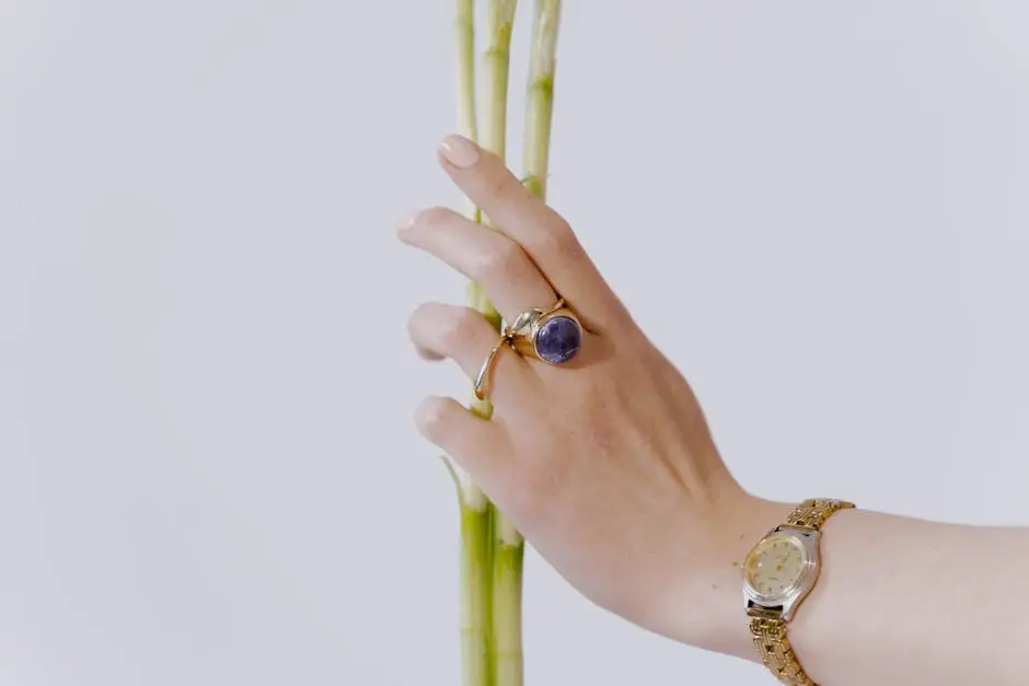 A graceful hand with a ring and watch gently holds a green bamboo stalk.