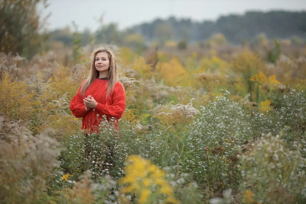 Woman in red sweater standing in a serene autumn field with wildflowers.