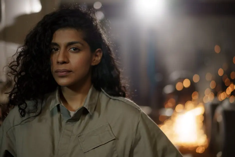 A confident woman in coveralls stands in a workshop, embodying empowerment and skill in a traditionally male-dominated field.