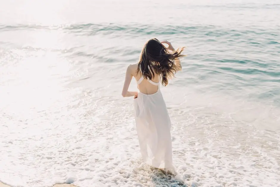 A woman in a white dress walking on a sunny beach enjoying the sea waves.