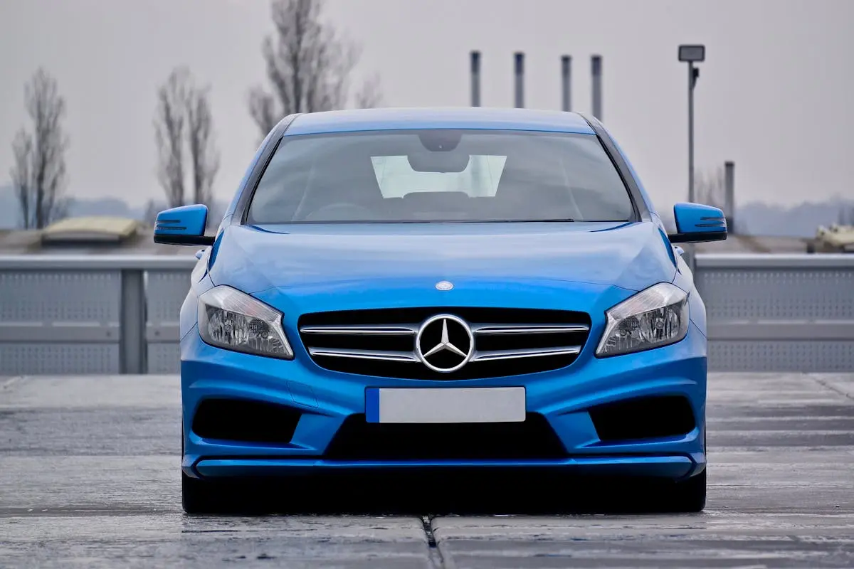 Front view of a blue Mercedes-Benz car parked on a wet street under cloudy skies.