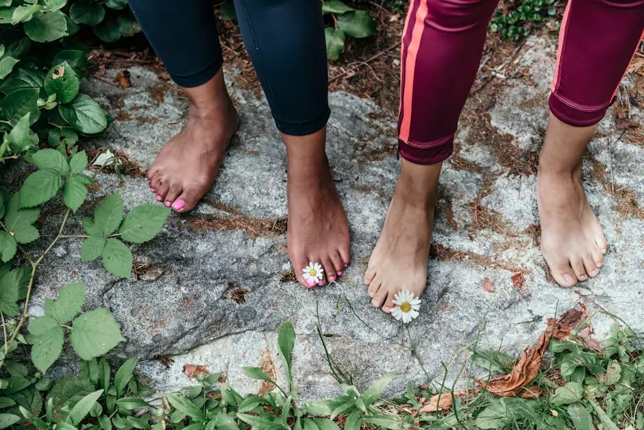 Two people standing barefoot on rocky ground with daisies on toes outdoors.