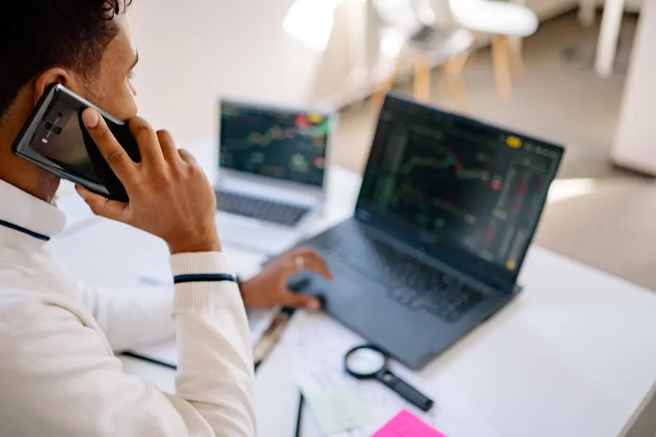 A Man Having a Phone Call while Looking at the Graph on the Monitor of His Laptop