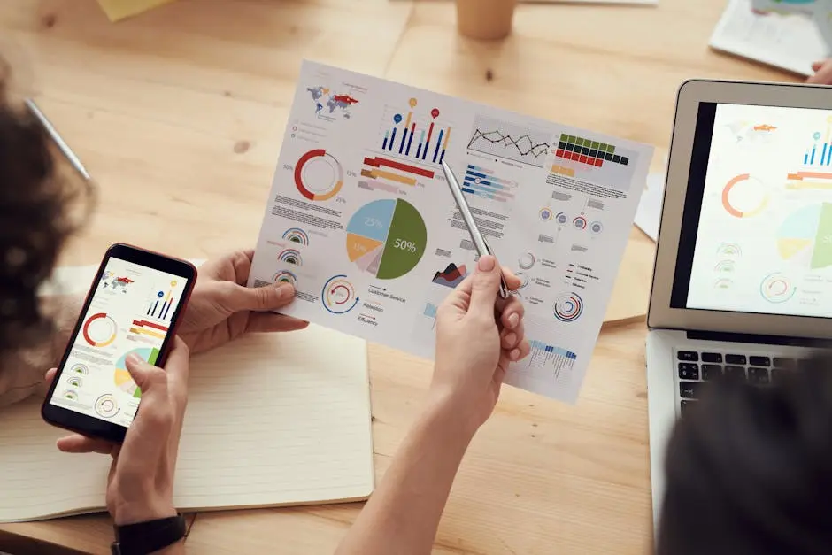 Team members analyze charts during a business meeting with laptops and smartphones.