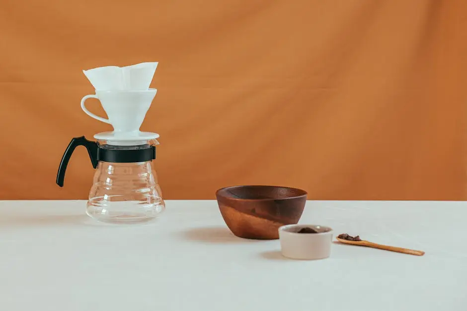 A Glass Pour-Over Coffee Maker on a White Surface Beside a Wooden Bowl