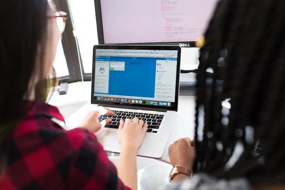 Two women working together on a laptop in a bright, modern office setting.