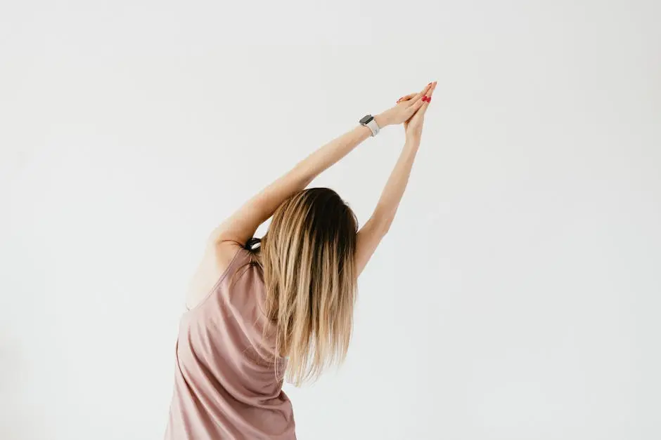 Back view of anonymous young female in active top stretching rib cage with raised arms during workout