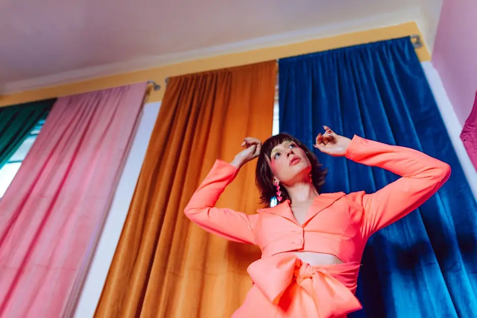 Woman in Pink Long Sleeve Dress Standing Near Orange Curtain