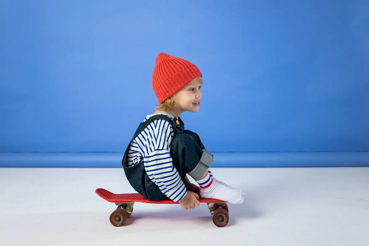 Child in Black and White Striped Long Sleeve Shirt and Red Knit Cap Sitting on Brown