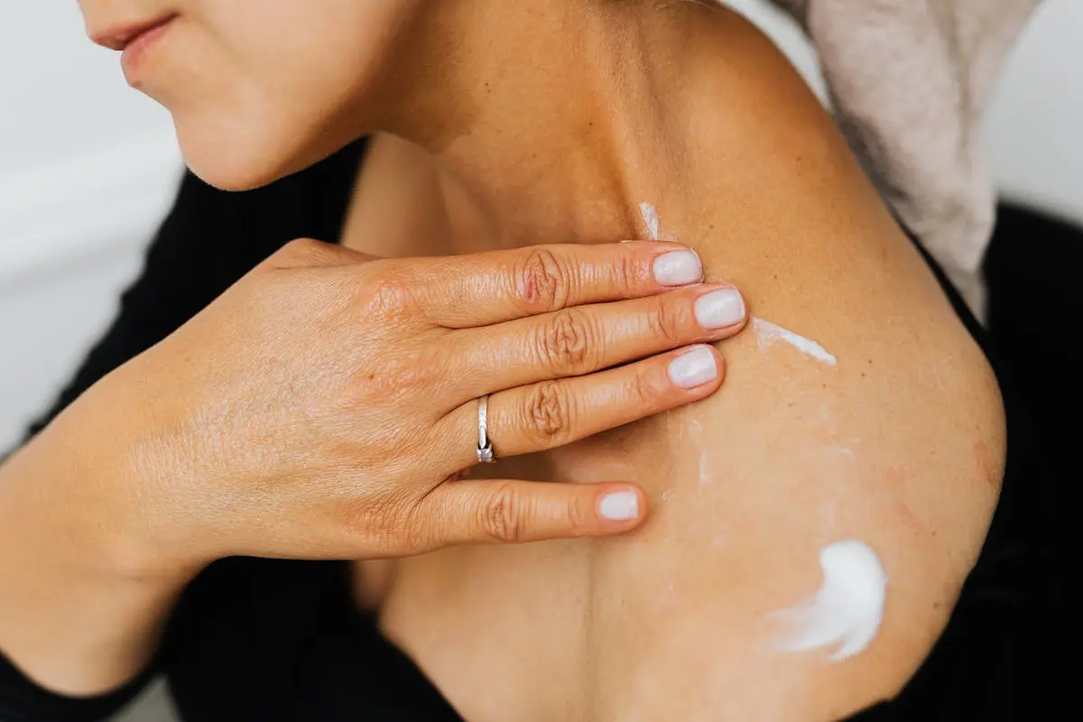 A close-up image of a woman applying skincare lotion on her neck with manicured hands. elegant jewelry