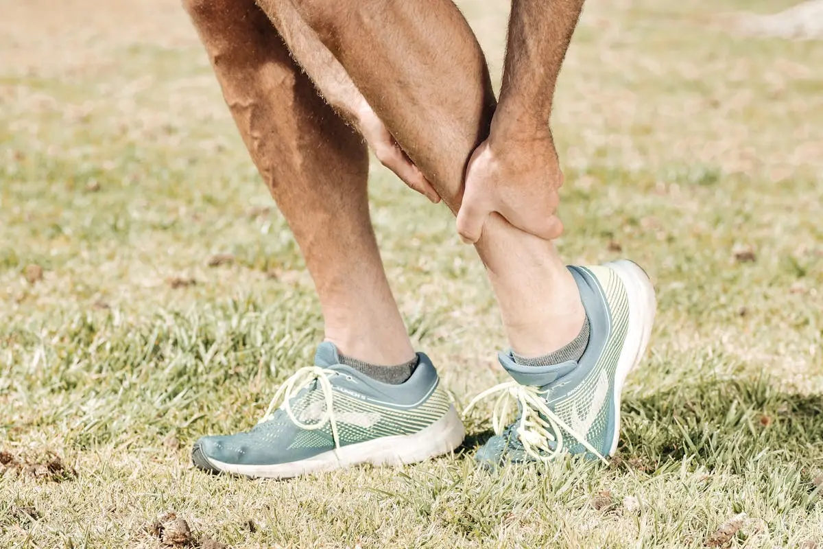 Man holding his calf in pain, wearing teal sneakers on green grass.