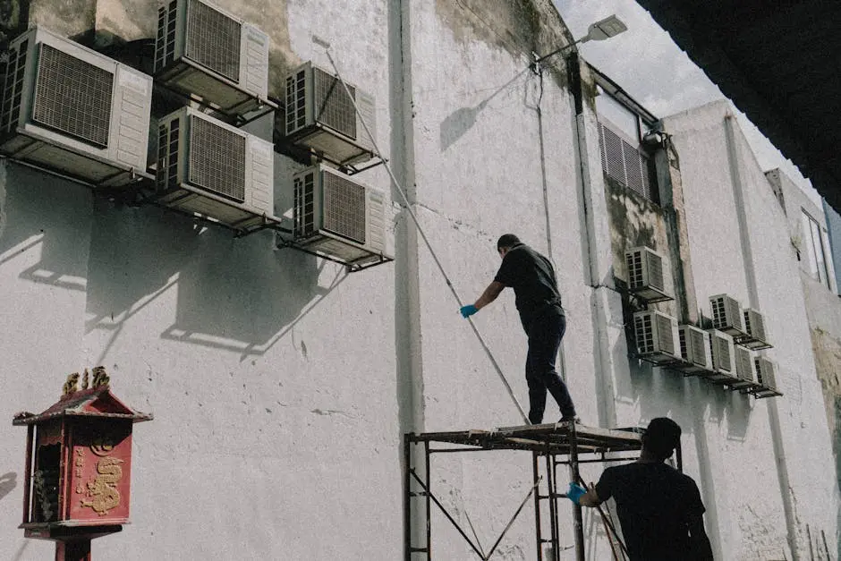 A man on a ladder cleaning air conditioners on a wall