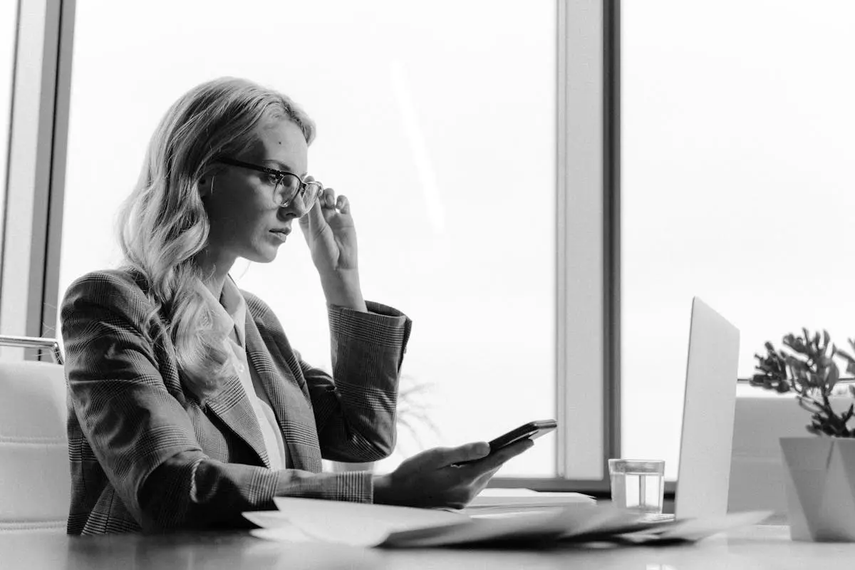 Grayscale Photo of Woman Holding Cellphone While Looking at the Screen of a Laptop