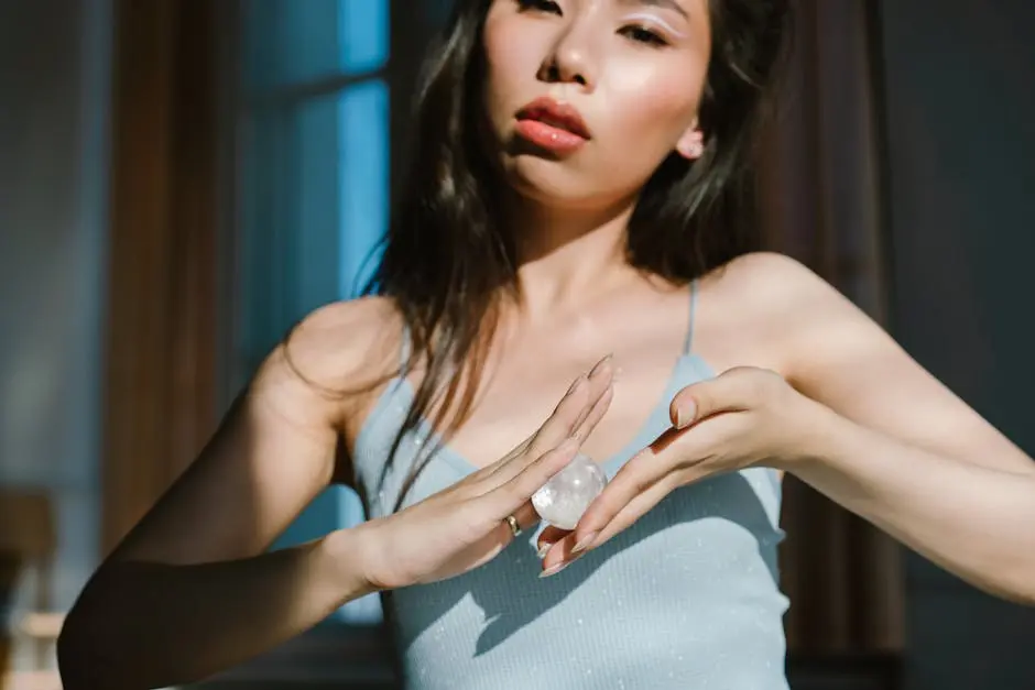 A serene woman holds a crystal indoors, basking in warm sunlight, emphasizing tranquility and spiritual energy.