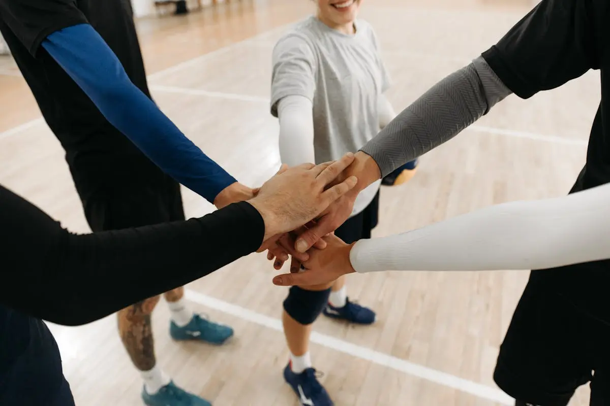 A group of athletes uniting with a hand stack in a sports setting, symbolizing teamwork.