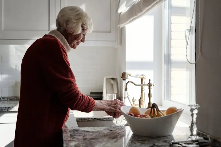 An Elderly Woman Washing Fruits in the Kitchen Sink