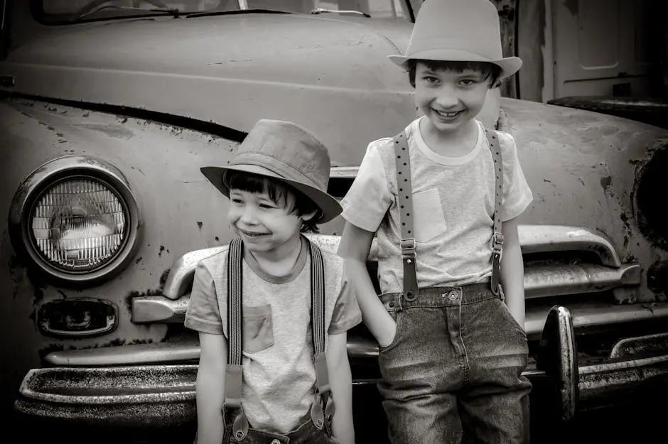 Two happy boys wearing hats and suspenders stand in front of a retro car, smiling.