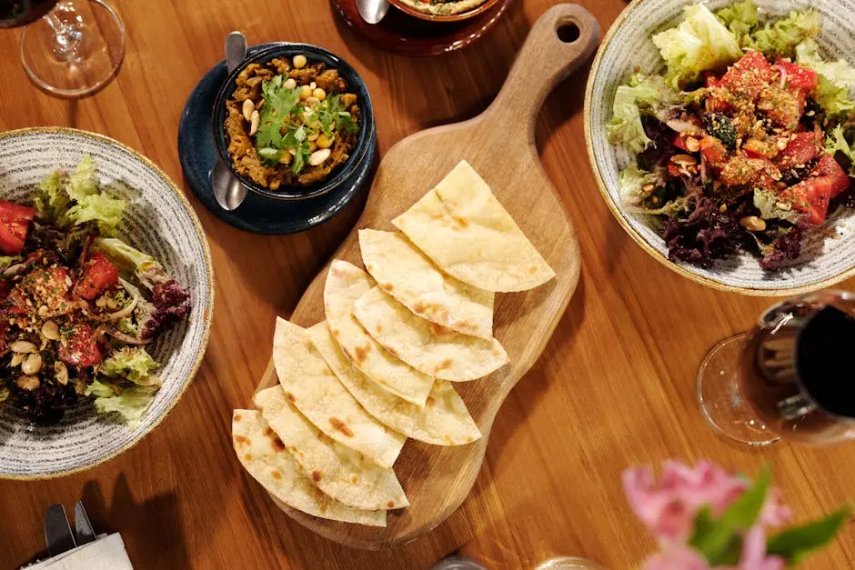 A colorful Mediterranean spread featuring pita, salads, and wine on a wooden table.