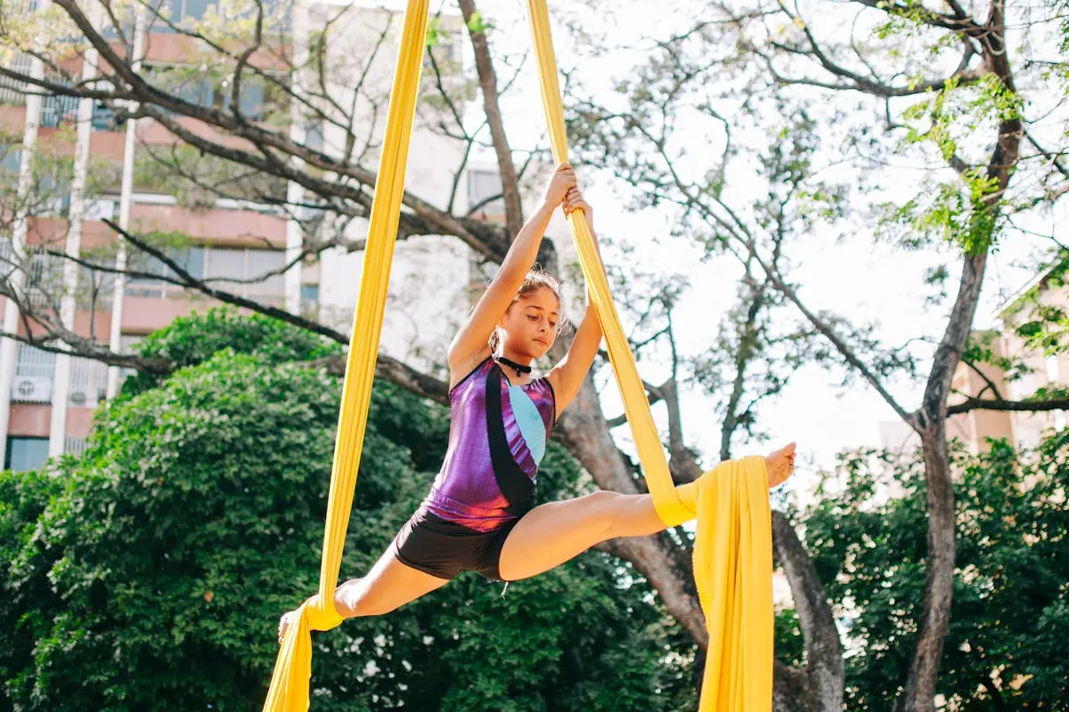 A young girl gracefully performs aerial silks in an outdoor park setting.