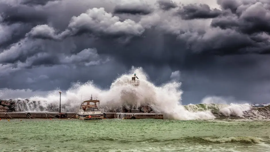 Powerful waves crash against a pier and lighthouse under dark stormy skies.