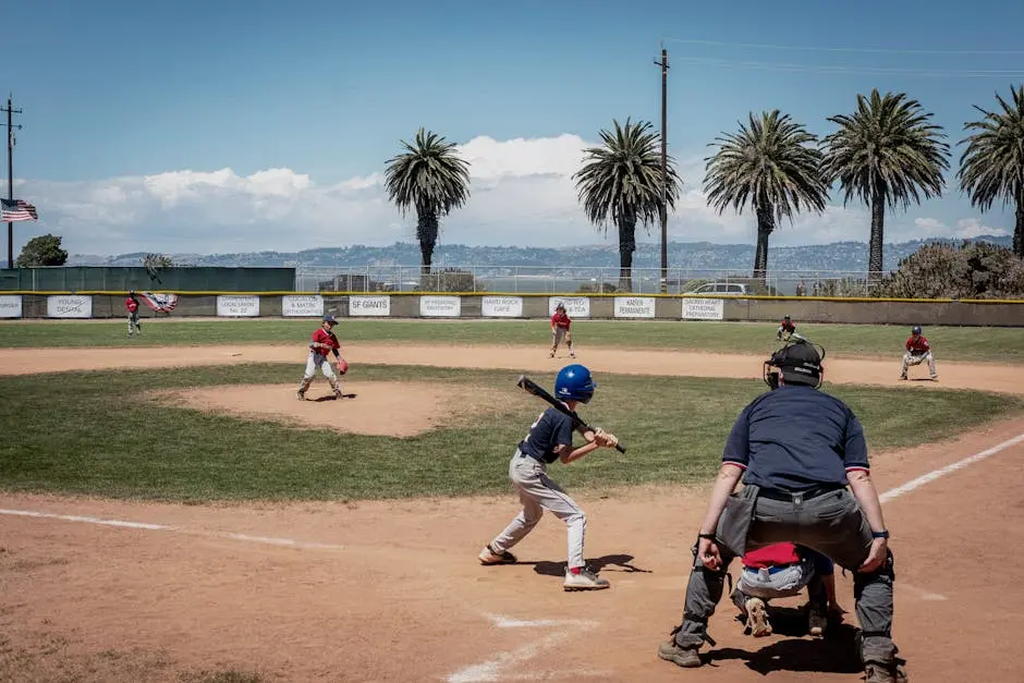 Kids playing baseball on a sunny day at a scenic field with palm trees and mountains.