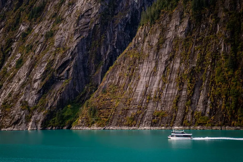 A scenic cruise boat navigates through an Alaskan fjord with towering cliffs, showcasing nature’s grandeur.