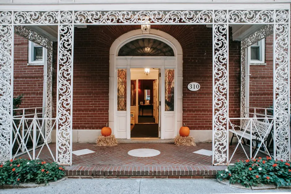 Exterior of residential brick building with doorway and white ornamental veranda with metal barriers located on street with blooming flowers