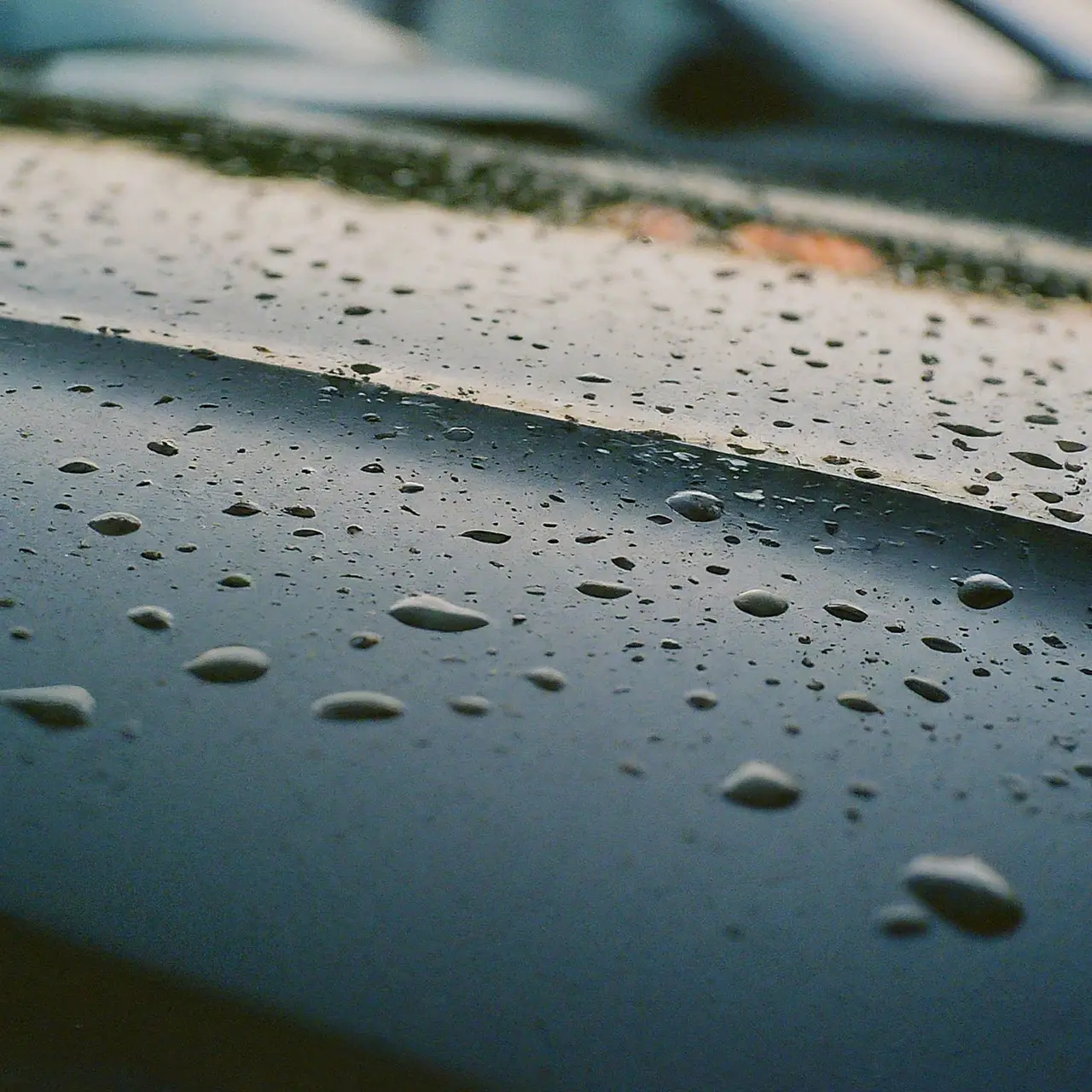 A glossy car hood with a water droplet rolling off. 35mm stock photo