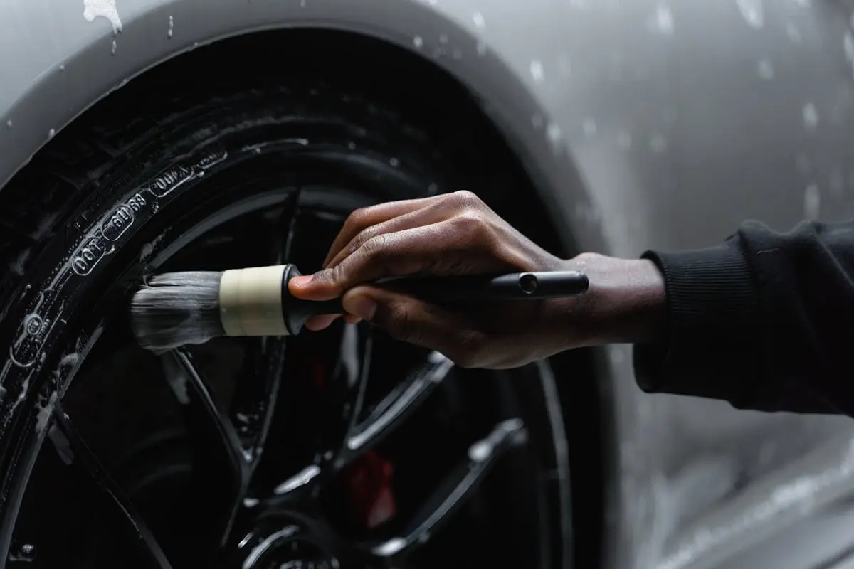 A detail-oriented close-up of a hand cleaning a car tire with a brush and soap.