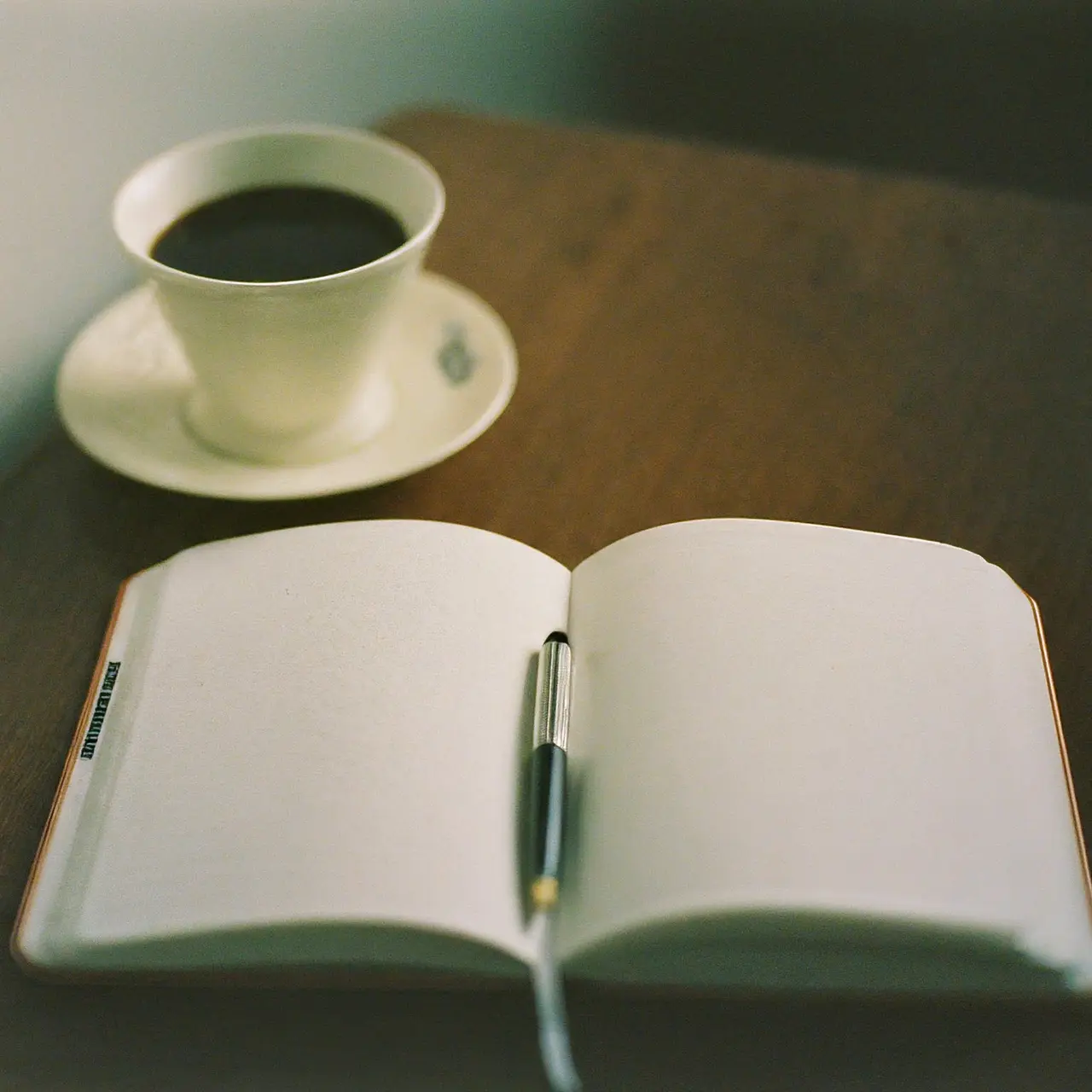 An open notebook, pen, and coffee cup on a desk. 35mm stock photo