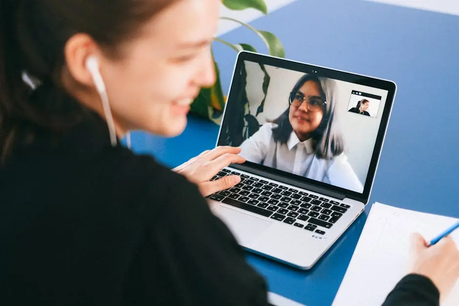 Woman having a video conference on a laptop, smiling and taking notes.