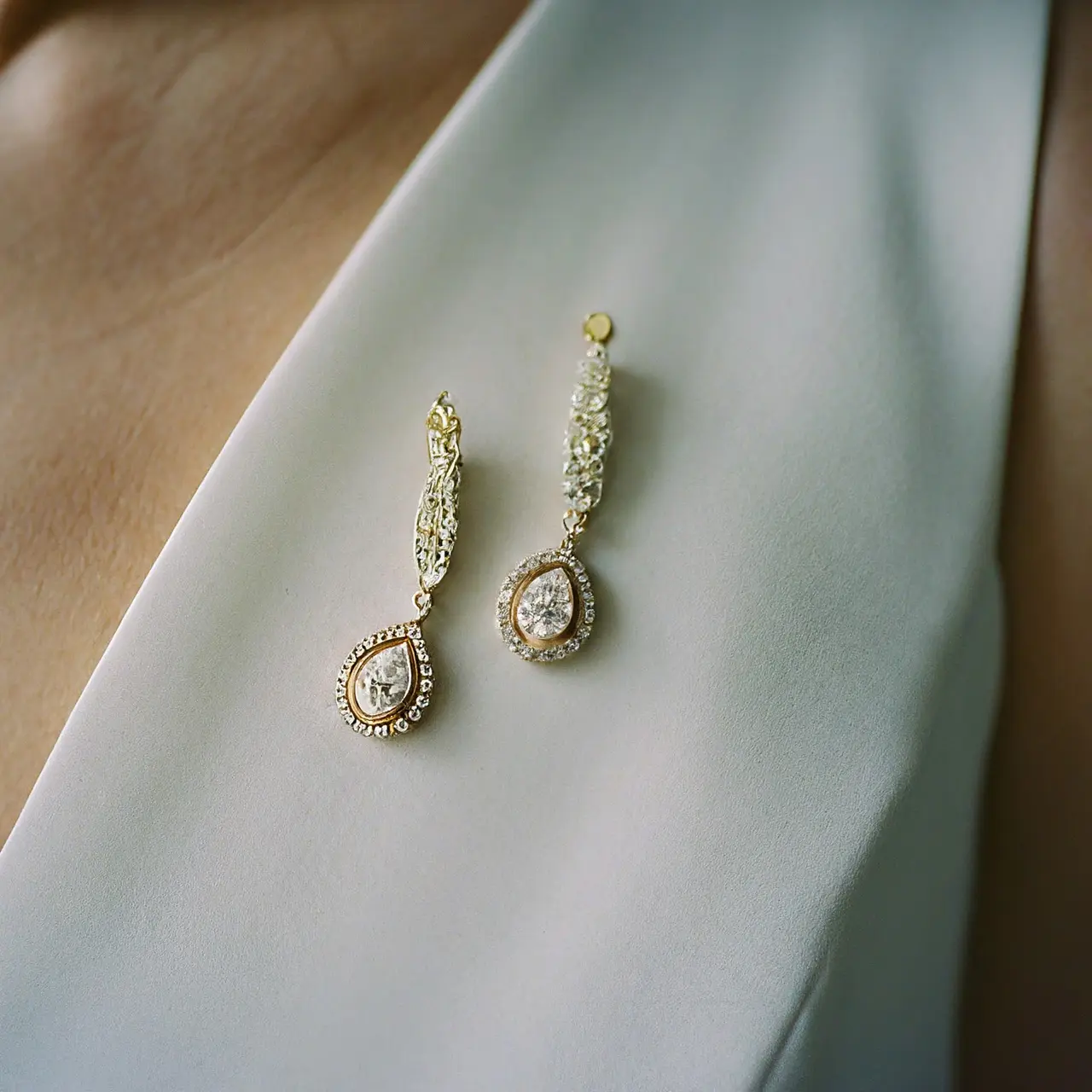 Gold diamond earrings next to an elegant white wedding dress. 35mm stock photo