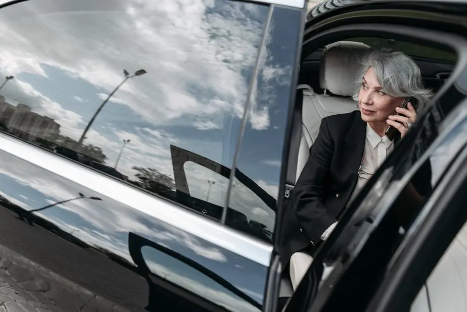 Senior woman with grey hair in a car, dressed professionally, making a phone call.