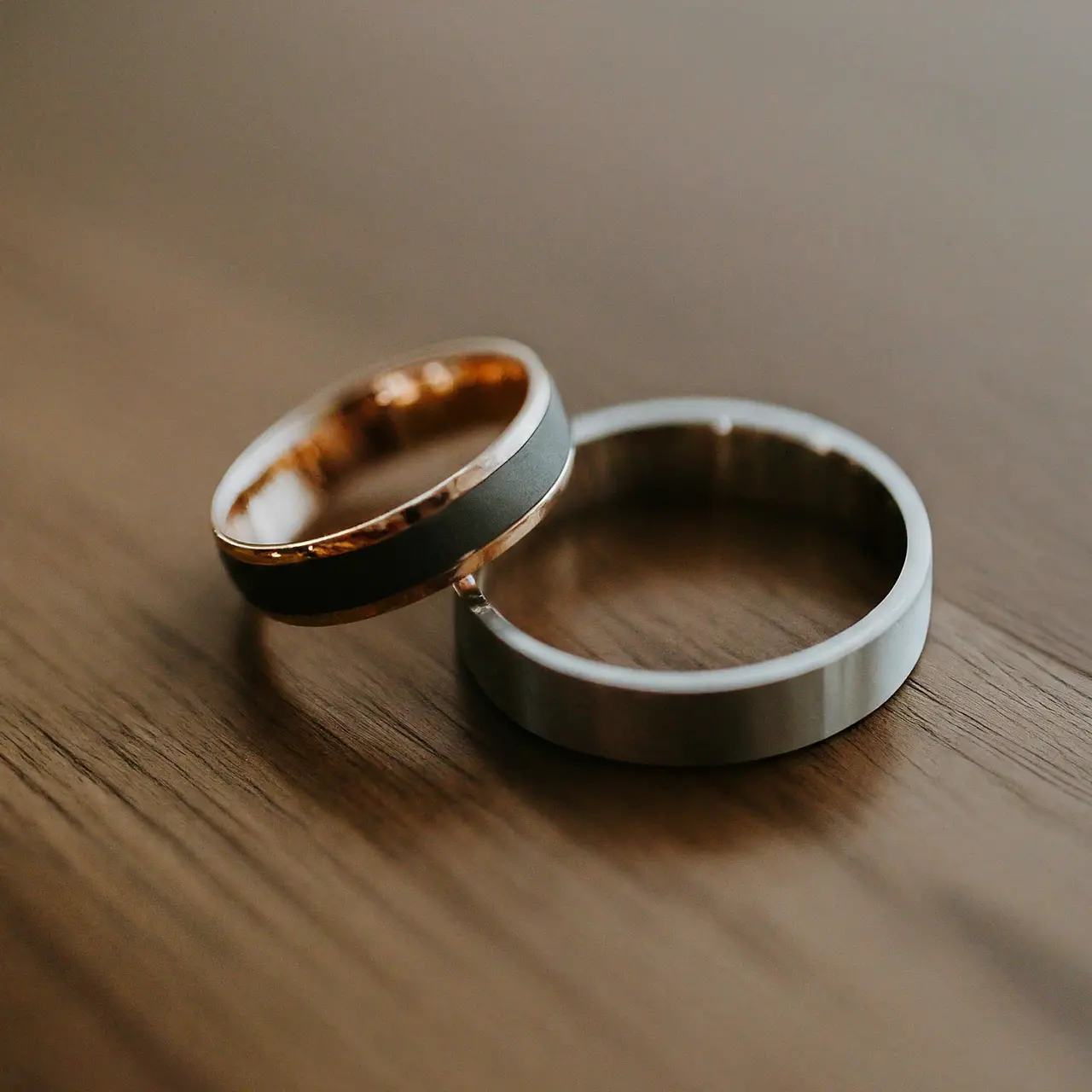 Two contrasting men’s wedding bands on a wooden surface. 35mm stock photo