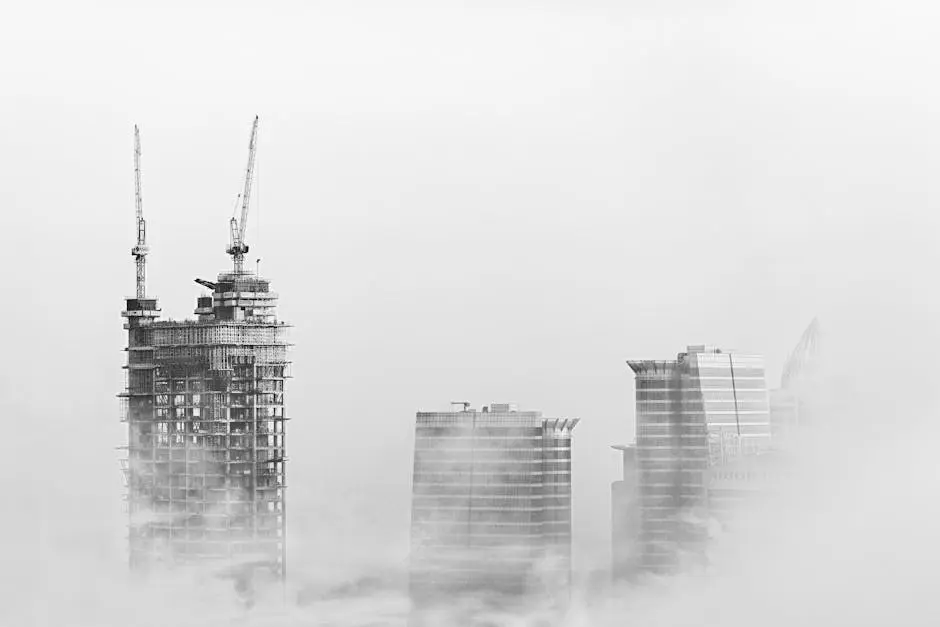 Black and white photo of Dubai skyline with skyscrapers and cranes emerging from fog, showcasing urban development.