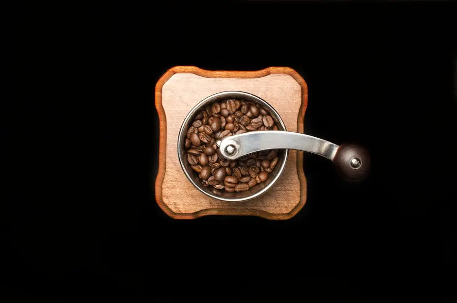 Close-up photo of roasted coffee beans in a wooden manual grinder on a dark background.