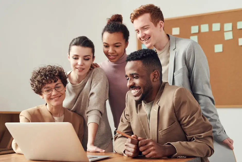 A group of diverse young professionals happily collaborating around a laptop indoors.