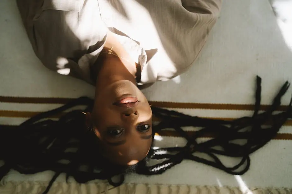 Serene portrait of a woman with afro braids lying indoors in soft lighting.