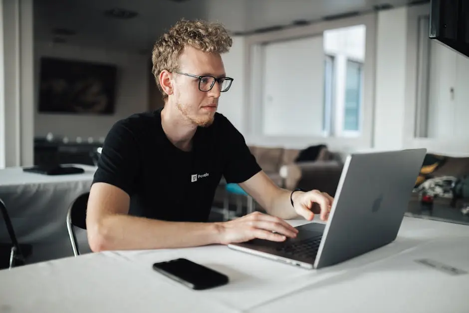 A focused young man working on a laptop in a modern office setting, highlighting productivity and technology.