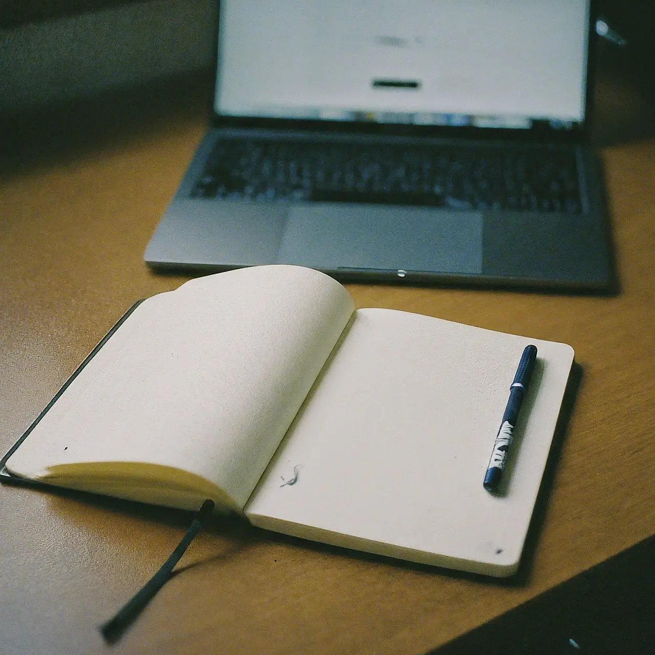 A laptop, open notebook, and pen on a tidy desk. 35mm stock photo