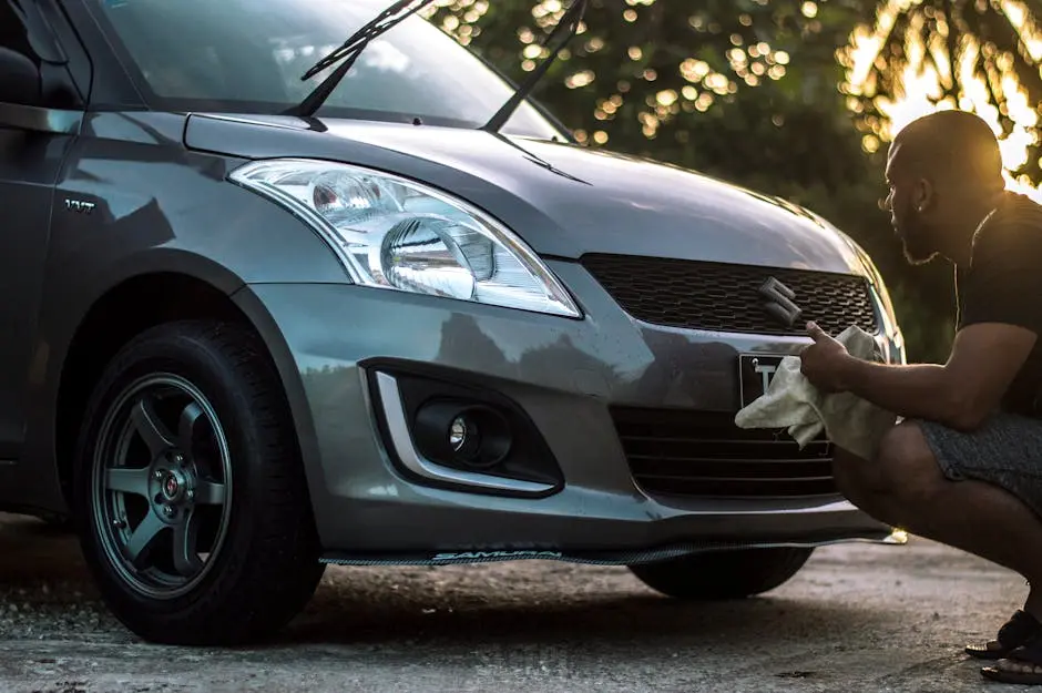 A man carefully cleans a car hood at sunset, focusing on details.