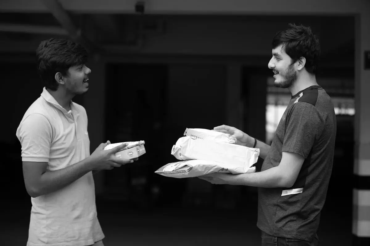 Monochrome image of two adult male friends exchanging packages indoors.