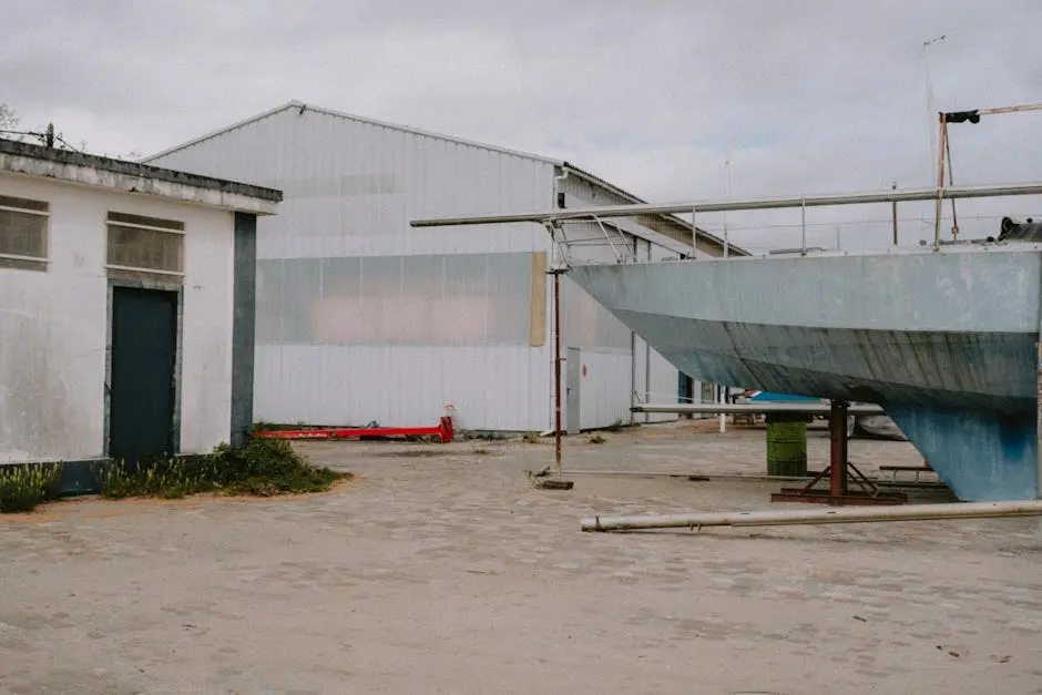 A deserted shipyard featuring a dry docked boat near industrial buildings under overcast sky.